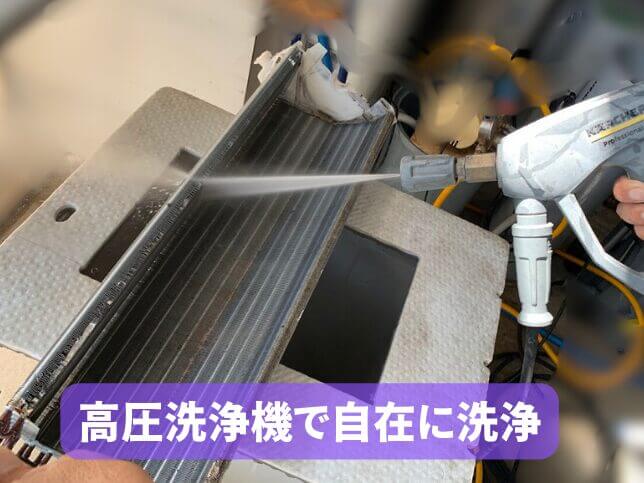 エアコン完全分解クリーニングで熱交換器を高圧洗浄機で洗浄している様子。画面下には「高圧洗浄機で自在に洗浄」と表示。